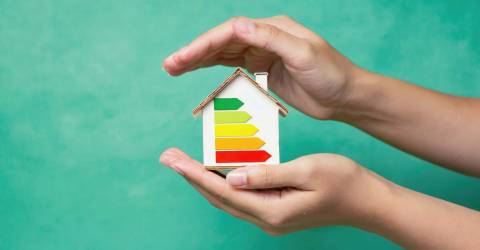 Verduurzamen, Energiebesparing; een huisje met energielabels wordt tussen 2 handen gehouden op een groene achtergrond