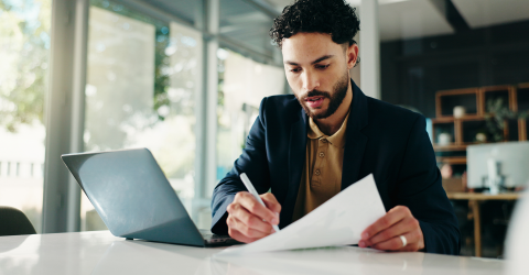 Man achter een bureau met laptop voor zich en een pen en document in zijn is een controle aan het uitvoeren